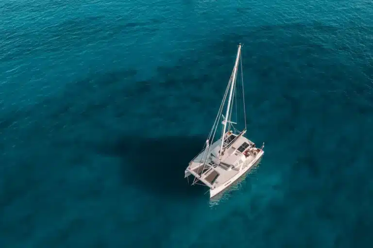 Luftaufnahme eines weißen Segelboots auf einem ruhigen blauen Ozean. Die Aufnahme zeigt einen deutlichen Kontrast zwischen dem Boot und dem tiefblauen Wasser, das es während eines Segelurlaubs umgibt.