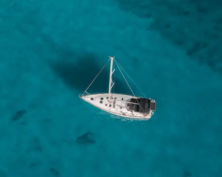 Luftaufnahme eines weißen Katamarans, der auf klarem, türkisfarbenem Wasser schwimmt.