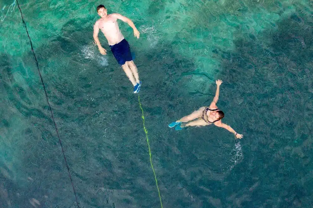 Luftaufnahme von zwei Personen beim Schnorcheln im klaren, türkisfarbenen Wasser, einer treibend frei und der andere an einem Sicherheitsseil befestigt während eines Segelurlaubs.