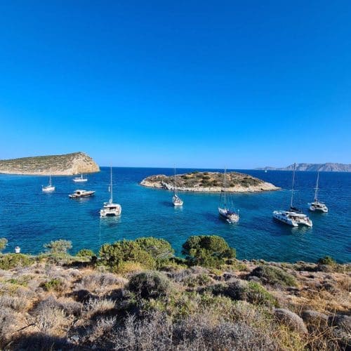 Segelboote ankerten in einer klaren, blauen Bucht, umgeben von felsiger Küste und mediterraner Vegetation unter einem strahlend blauen Himmel, perfekt für einen Segeltörn.