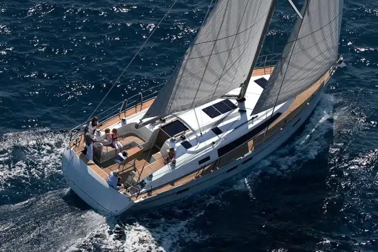Luftaufnahme einer luxuriösen Segelyacht, die auf dem Meer kreuzt, mit einer Gruppe von Menschen, die an Deck entspannen. Dabei werden das elegante Design und das geräumige Äußere der Yacht zur Schau gestellt.