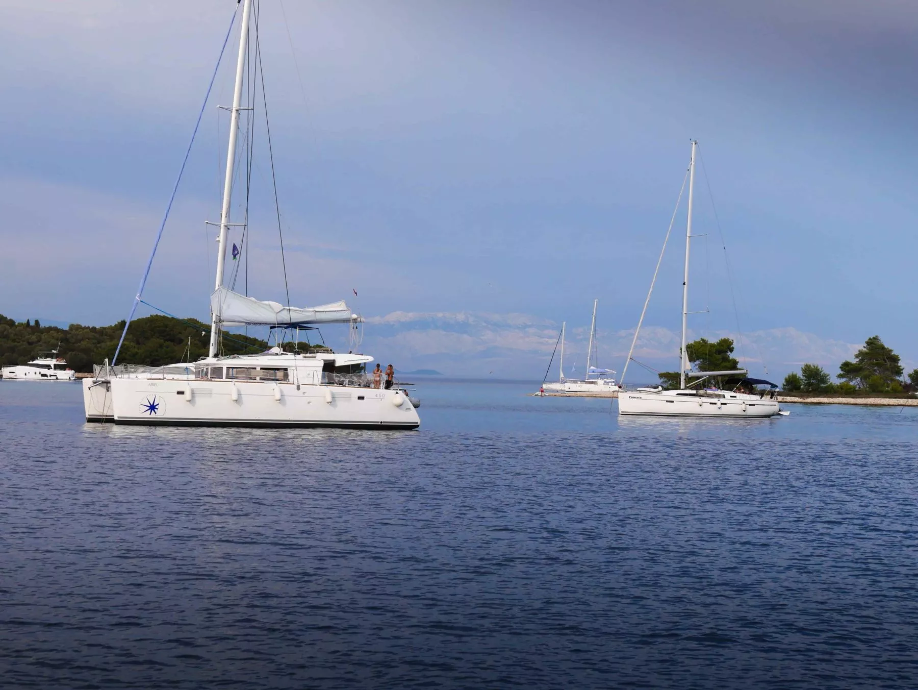 Zwei Segelboote ankerten in der Nähe einer kleinen Insel mit üppigem Grün in ruhigem blauen Wasser, unter einem klaren Himmel mit fernen Bergen im Hintergrund, bereit für eine Segelreise.