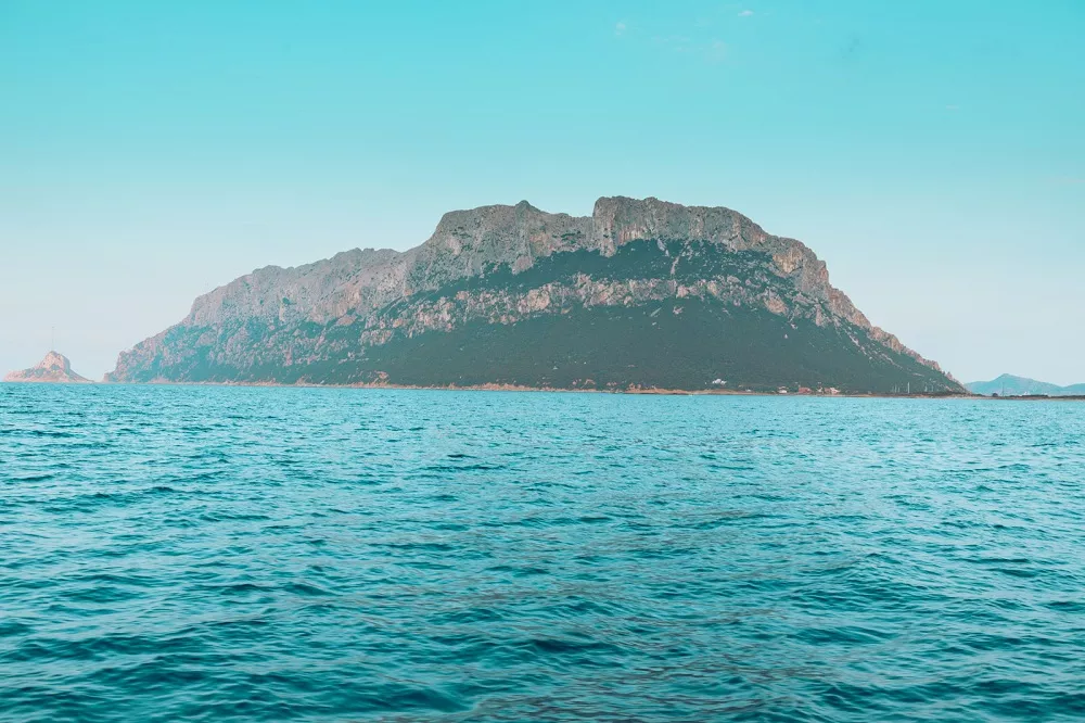 Ein Panoramablick auf einen großen, schroffen Berg, der sich während eines Segeltörns unter klarem Himmel aus dem Meer erhebt.