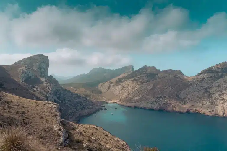 Ein Panoramablick auf eine ruhige Bucht, umgeben von schroffen Bergen unter einem teilweise bewölkten Himmel. Das klare türkisfarbene Wasser liegt eingebettet in das bergige Gelände, perfekt für eine Segelreise.