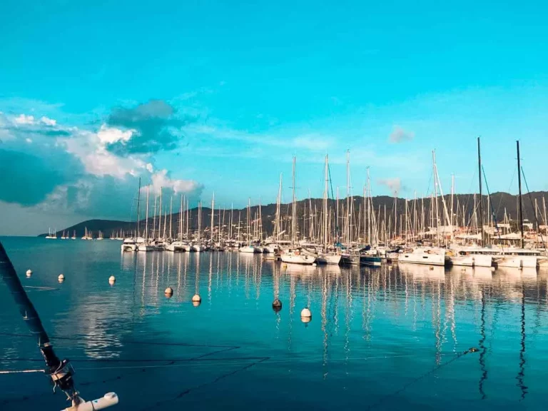 Ein ruhiger Yachthafen voller zahlreicher Segelyachten, die ordentlich vor dem Hintergrund eines blauen Himmels und der Berge in der Ferne bei Sonnenuntergang vor Anker liegen.