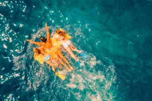 Luftaufnahme von vier Personen, die auf einem leuchtend gelben Schlauchboot im klaren, blauen Ozean treiben und während ihres Segelabenteuers ein dynamisches Plätschern um sich herum verursachen.