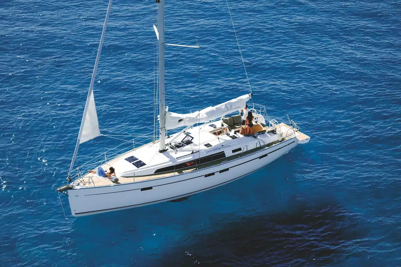 Ein weißes Segelboot mit gesenkten Segeln, das auf einem klaren, blauen Meer kreuzt, von oben betrachtet, bereit für eine Segelreise.
