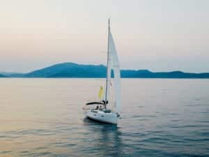 Ein heiteres Segelboot auf ruhigem Wasser in der Abenddämmerung, mit sanften Hügeln im sanften pastellfarbenen Hintergrund, die zum friedlichen Mitsegeln einladen.