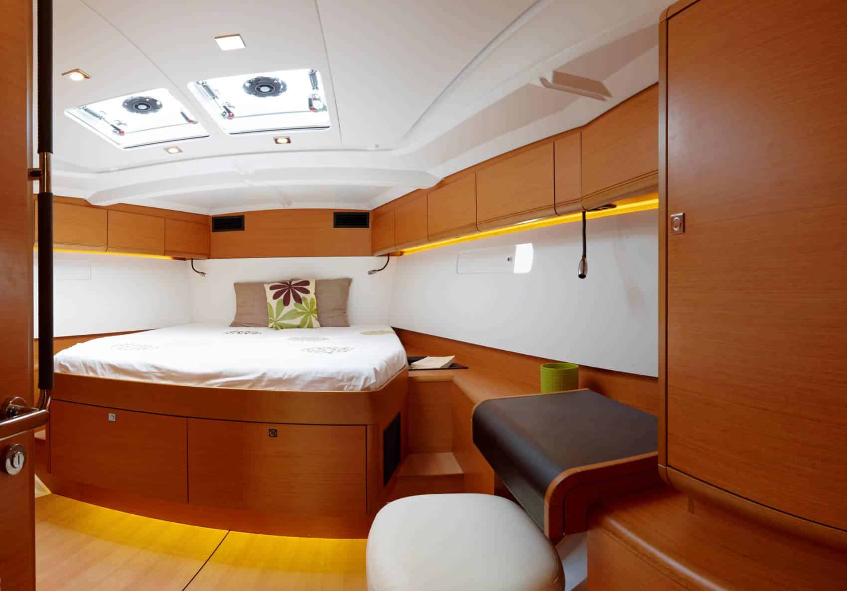 Innenansicht einer luxuriösen Segelyachtkabine mit einem großen Bett mit weißer Bettwäsche, Holzschränken und dezenter Beleuchtung, die ein gemütliches und elegantes Design zur Schau stellt.