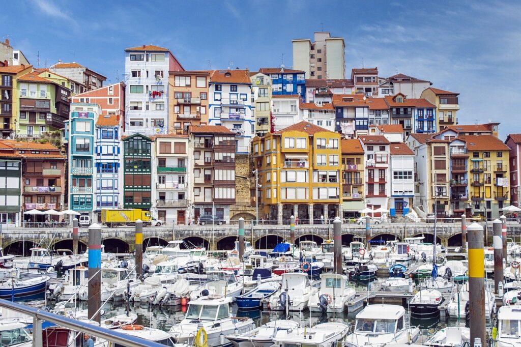 Eine malerische Hafenstadt ist zu sehen mit vielen bunten Häusern und kleinen Booten. Der historische Charme der Stadt kommt in dem Foto rüber, es wirkt fröhlich. Die Stadt befindet sich in Mallorca, perfekt für ein historisches Segelabenteuer. 