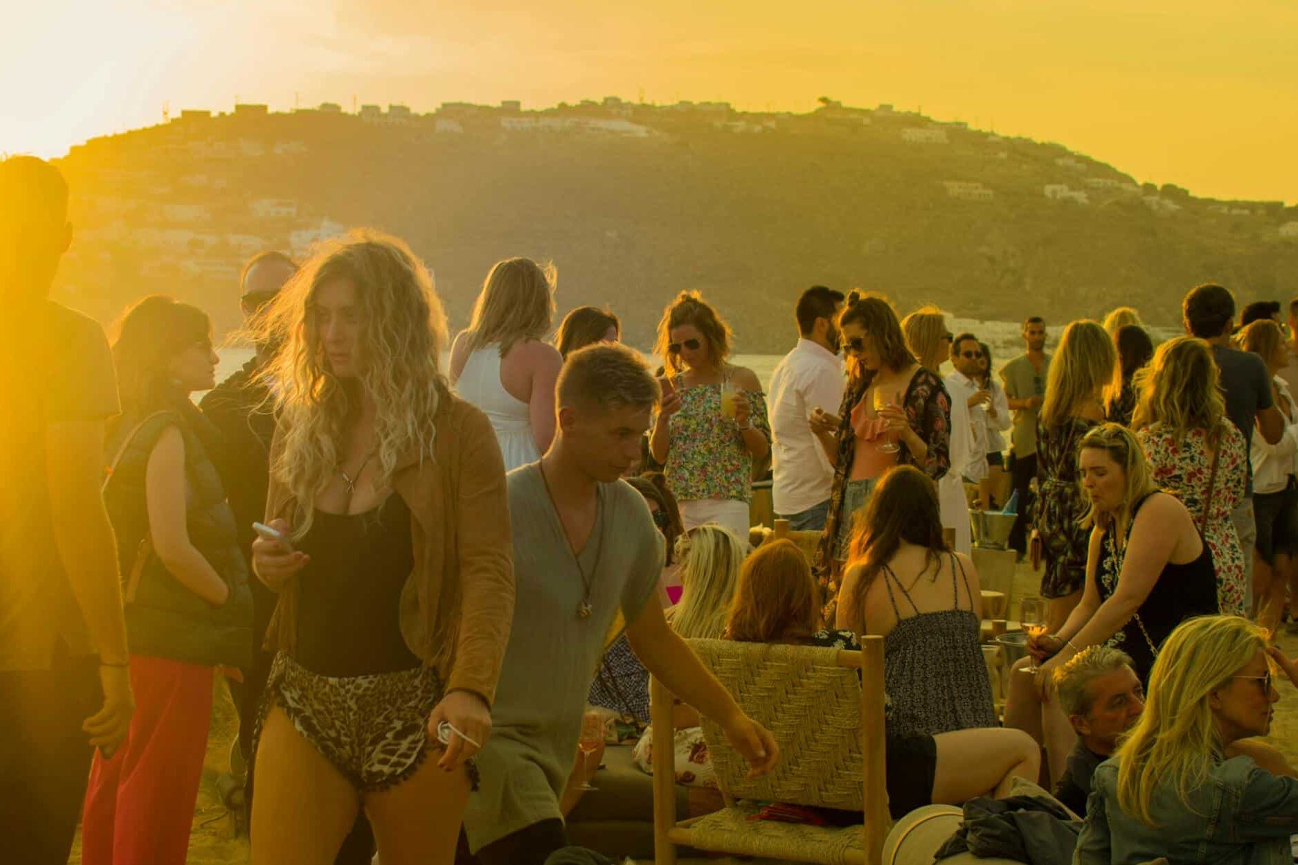 A lively gathering of people enjoying a sunset party on a beach in Mykonos, Greece. Junge Reisende