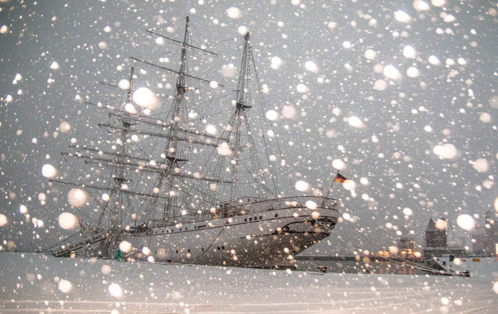 Sailing ship docked in snowy Stralsund harbor, Germany, during winter snowfall.